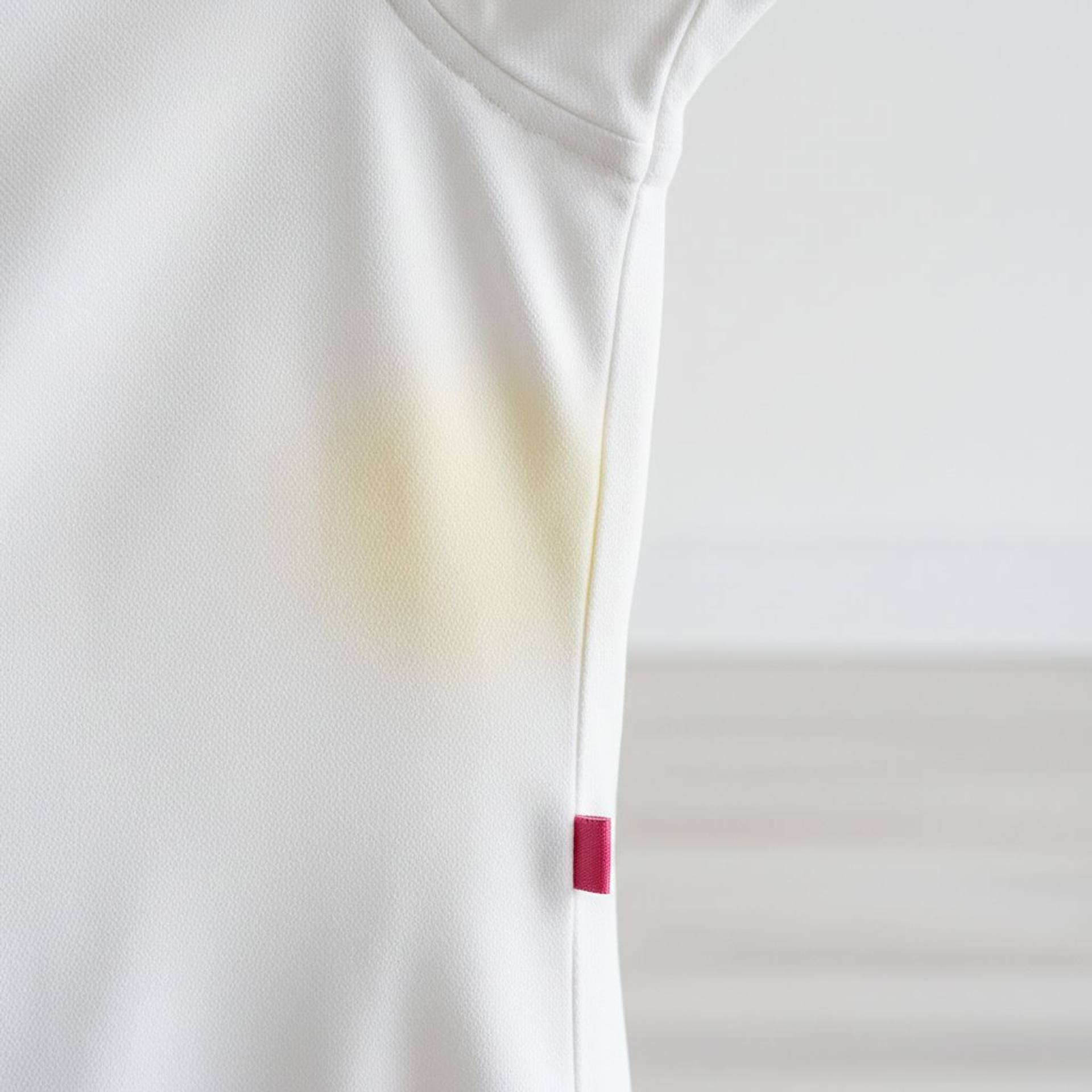 White shirt with visible yellowish stain under the arm on a bright laundry interior background.